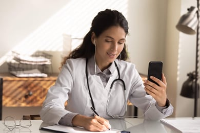 Doctor holding a phone, taking notes on a pad